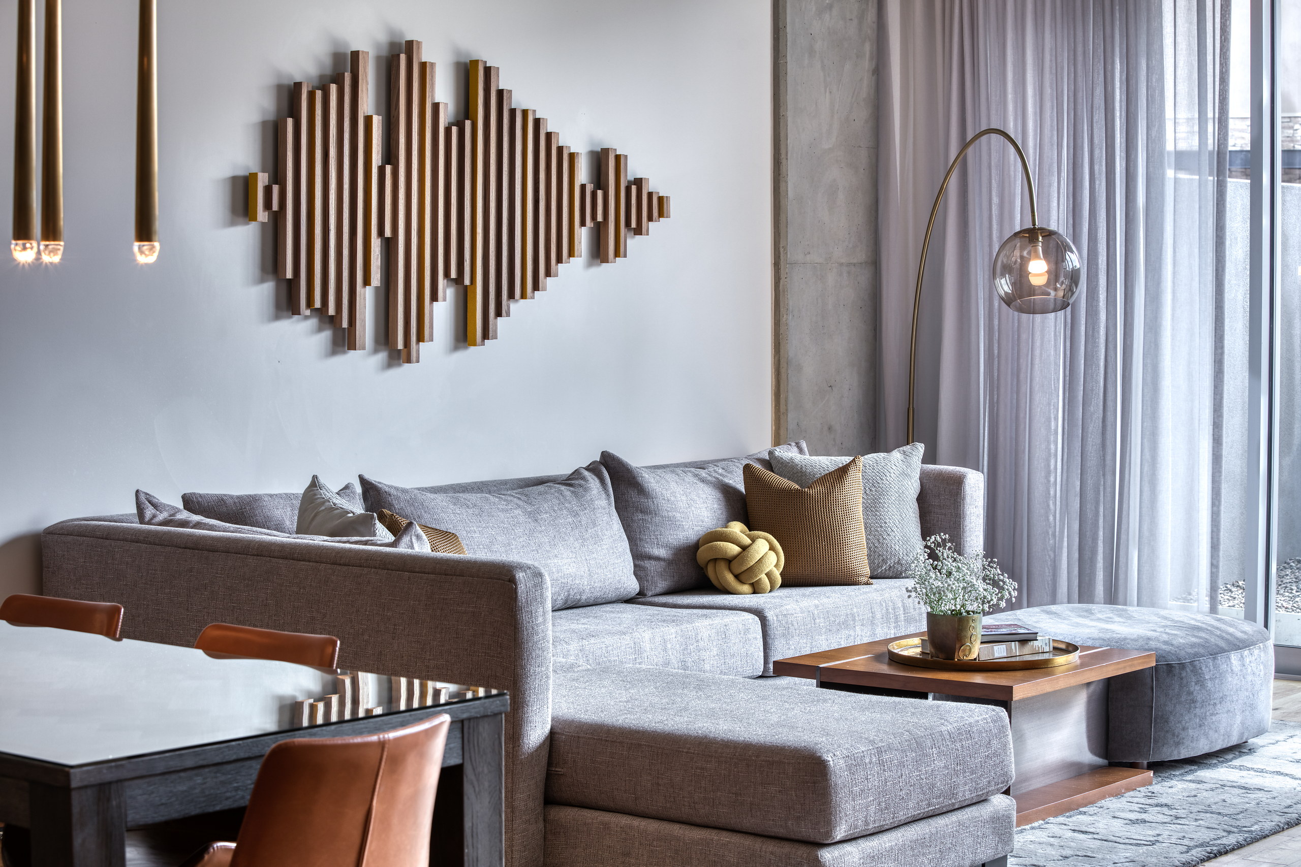 Gray modular sectional beneath a sculptural wood wall installation